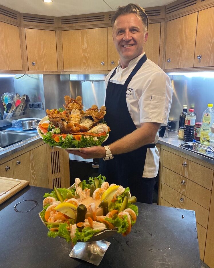 Hasan Emence standing behind two large serving arrangements in a kitchen.