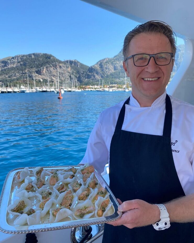 Hasan Emence holding a rectangular platter with the sea in the background.
