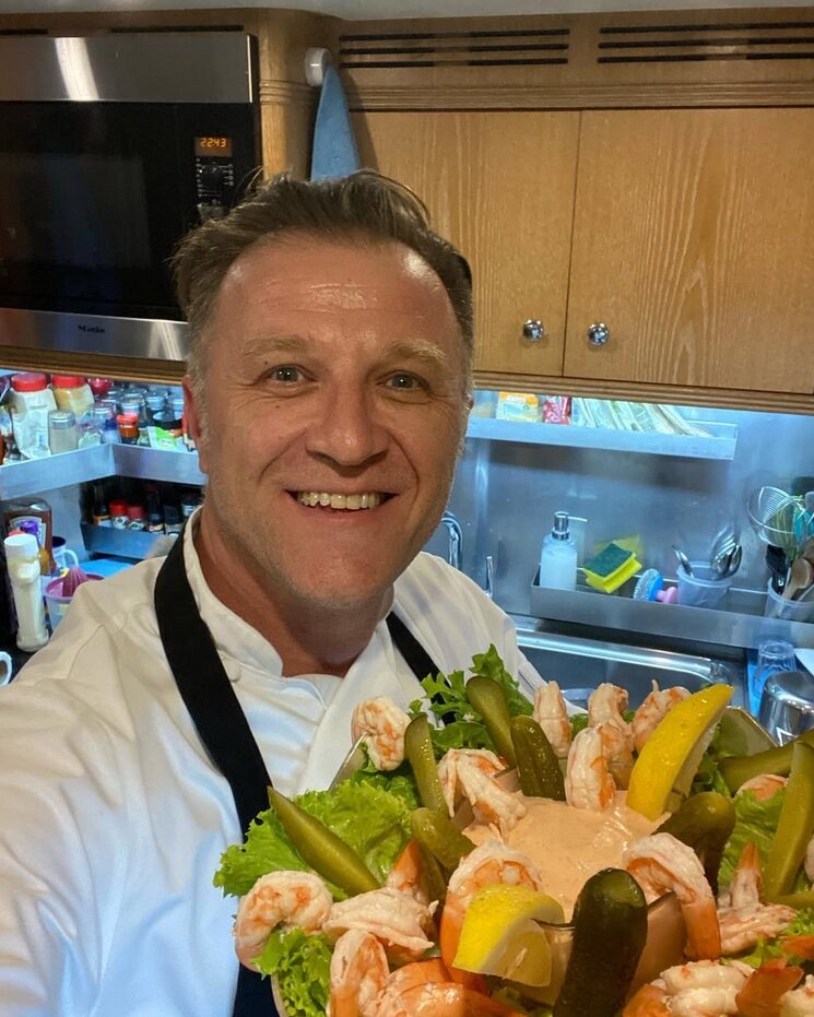 Hasan Emence smiling behind a large presentation platter in a kitchen.